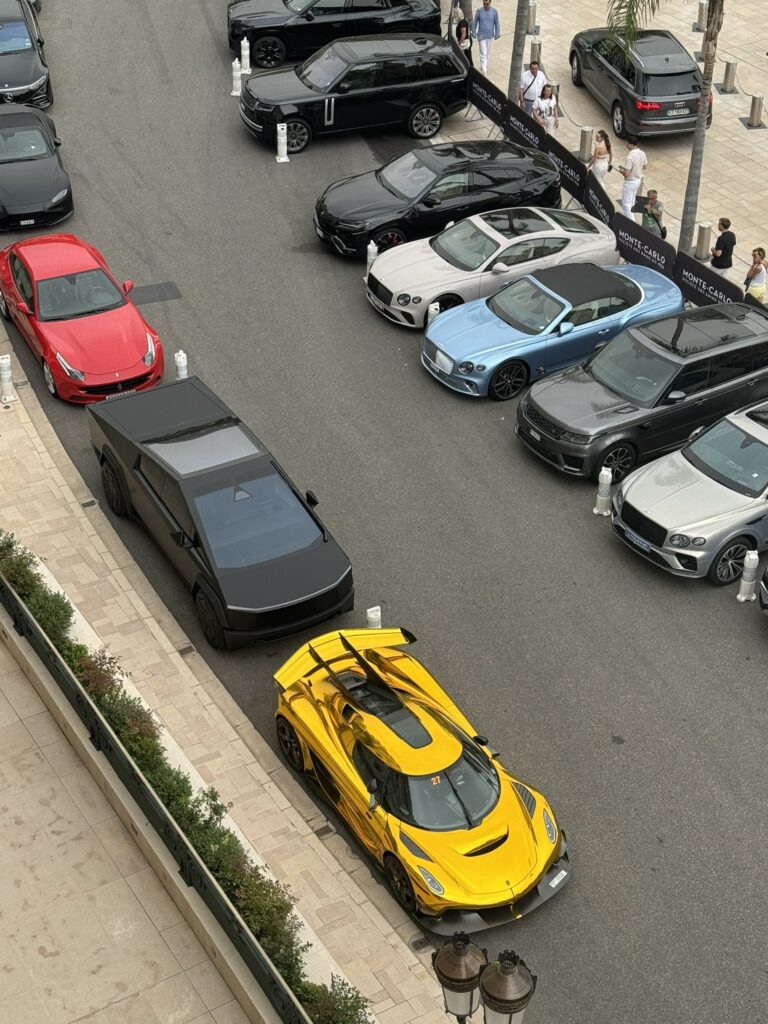 Matte Black Cybertruck parked in Monaco behind a golden Koenigsegg Jesko sports car.